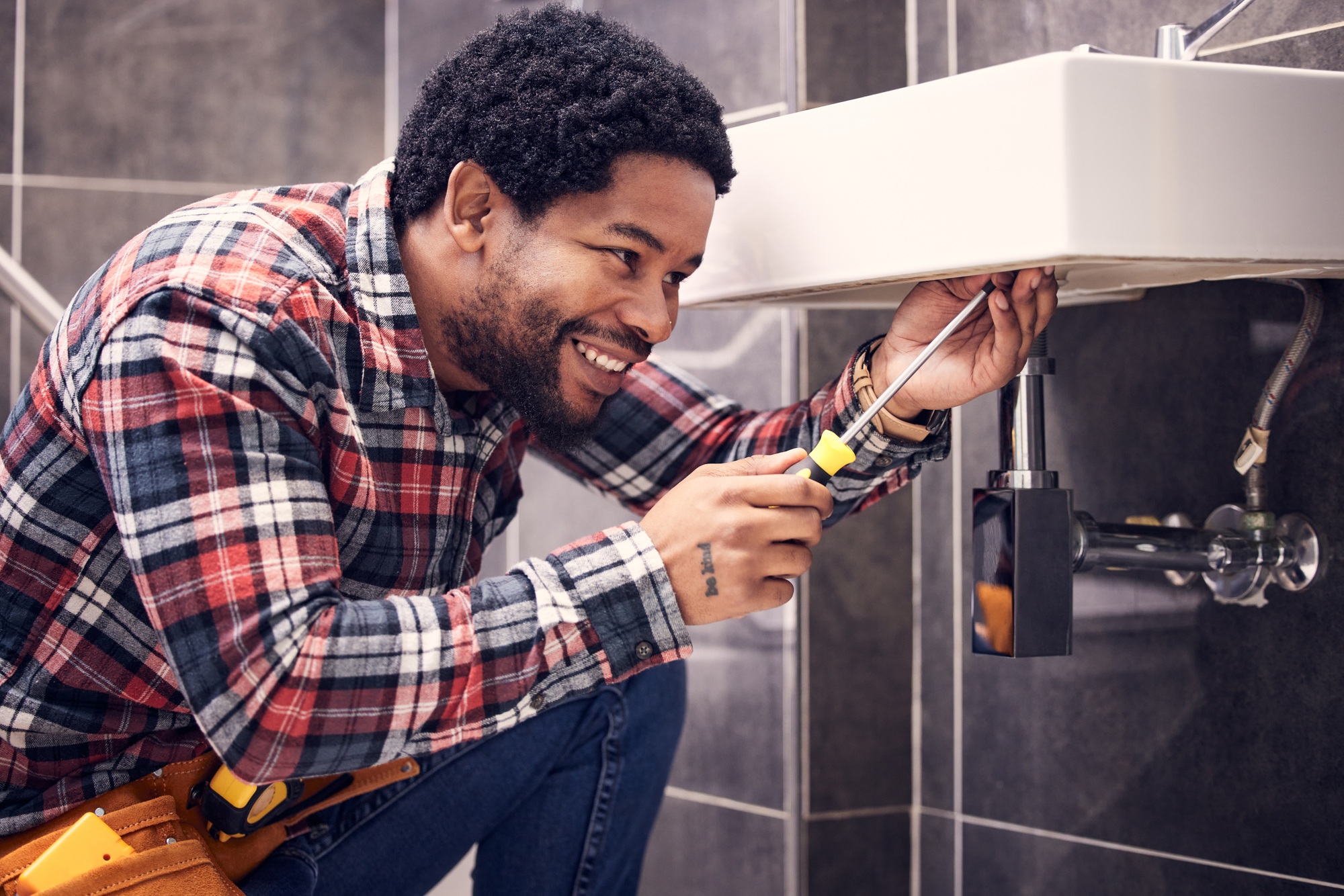 Happy, black man or plumber fixing a sink with smile in maintenance or installation with home repai